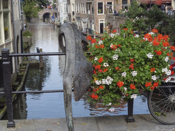 Sculpture and bicycle on a railing along a canal with blooming flowers and reflecting buildings, utrecht, Netherlands