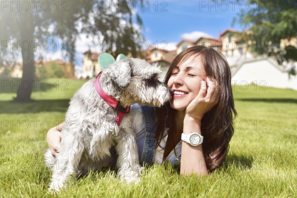 Pretty adult caucasian happy woman resting in the park on a sunny day with her beloved dog. Female lay on the grass smiling and looking at the camera