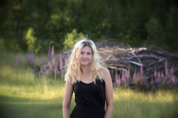 Portrait young blonde woman out and about in nature on a summer evening. Young woman with long blonde hair in summer nature