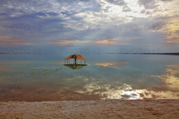 Winter in the Dead Sea. Excellent optical effects and reflections of clouds and sun in the water. Red gazebo in the water near the shore