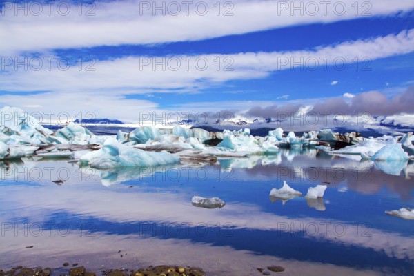 Clouds reflected in the smooth water of the largest glacial lagoon Jokulsaurloun. Iceland. Cold early summer morning. White and blue icebergs and ice floes. The concept of northern and photo tourism