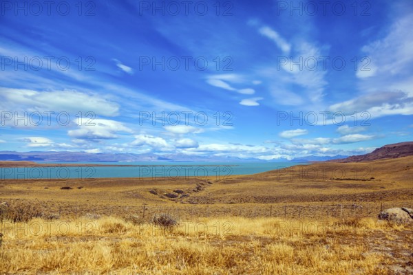 The concept of active and exotic tourism. Flat plain with shallow lake and yellowed grass. Patagonian Pampas. Strong wind carries clouds