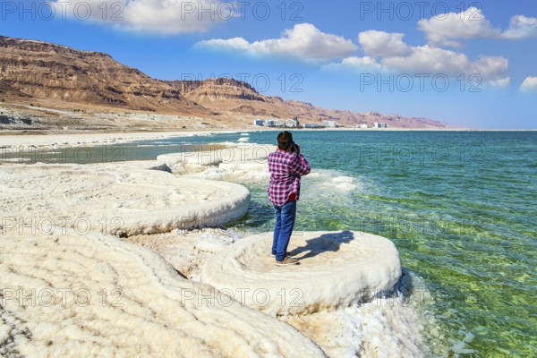 Woman in a plaid cowboy shirt photographs the sea surface. Evaporated salt forms beautiful crystals on the surface of the water. The saltiest lake in the world. Dead Sea. Israel