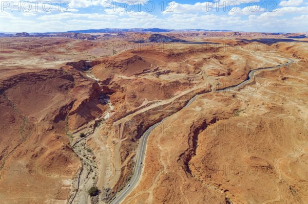Judean desert on the shores of the Dead Sea. Dry waterless hills of yelloy and beige clay. Magnificent road are laid among the hills. Shooting from a drone, from a bird's eye view. Israel