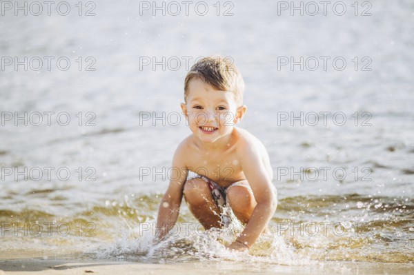 Theme is summer time and rest near the water. Little joyful Caucasian funny boy plays and enjoys in the river. The child is resting and swimming in the lake pond sandy beach