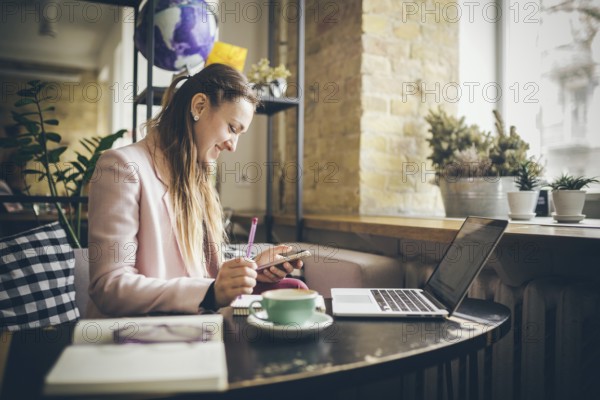 Successful business. Outsource. Woman blogger sits in cafe and uses smartphone, checks email, communicates with followers, reads news. Freelance blogger working, everywhere is a workplace concept