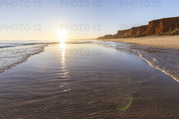 A landscape on the beach at low tide. The surrounding rocks and cliffs are reflected in the sea at sunset. Praia da Falésia, Algarve, Portugal
