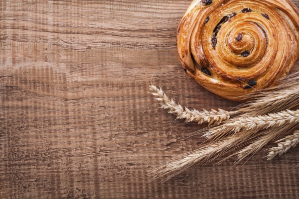 Sweet raisin bun bunch of wheat ears on oak wooden board food and drink concept
