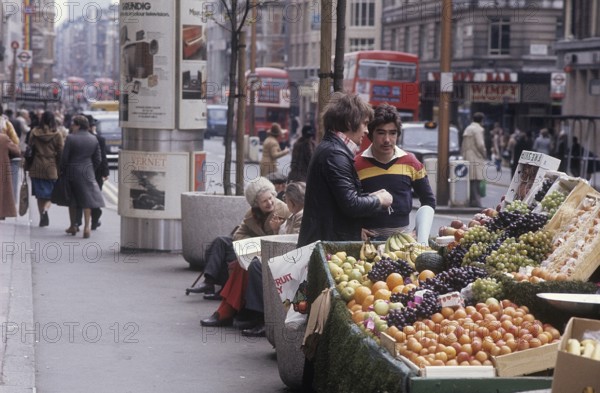 London 1982. A street view of a London street with a stand filled with fruit for sale. Credit Roland Palm