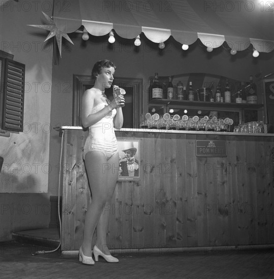 Woman in the 1950s. A young woman is standing in a bar with a drink in her hand sipping it with a straw. She is wearing clothes that from the theate or a variety show. Sweden 1956. ref Kristoffersson BE78-2