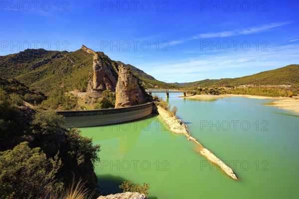 Picturesque conical rocks and a bridge over the reservoir. Magnificent dam collects the water of the Gallego River. Indian summer in northern Spain. Wonderful day
