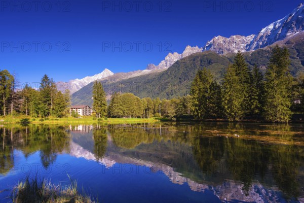 The mountain resort of Chamonix, Haute-Savoie. City Park is illuminated by the setting sun. The lake reflected the snow-capped Alps and evergreen spruce