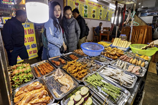 Visitors look at a rich selection of grilled food at a night market, restaurant in the streets of Sa Pa in Vietnam