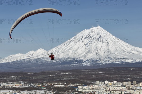 PETROPAVLOVSK-KAMCHATSKY, KAMCHATKA, RUSSIA, NOVEMBER 21, 2014: Paraglider flying over Petropavlovsk-Kamchatsky City on the background of the active Koriaksky Volcano on a sunny day