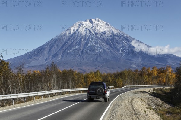 KAMCHATKA, RUSSIA, SEPTEMBER 30, 2012: Autumn view of car driving on road to active Koryaksky Volcano on Kamchatka Peninsula on sunny, cloudless day with blue skies. Russia, Far East