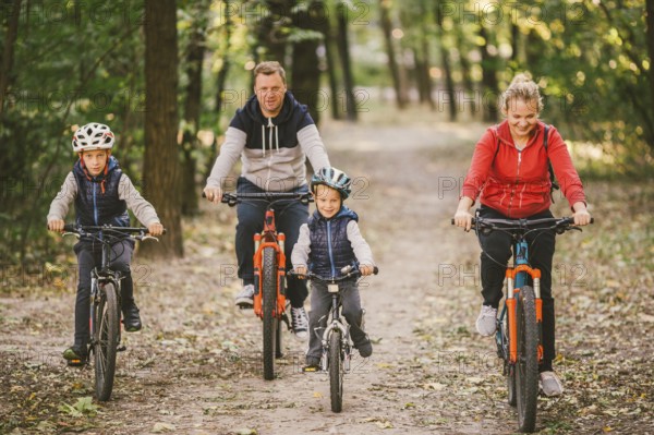 Parents and kids cycling on forest trail. family in warm clothes cycling autumn park. Family mountain bike on forest. active sports outdoor recreation. portrait Family Cycling Through Fall Woodland