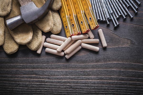 Wooden meter heap of dowels claw hammer leather protective gloves and metal nails on vintage wood board horizontal view construction concept