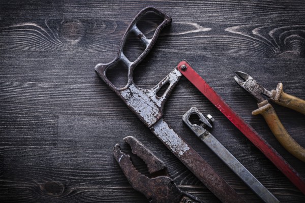Obsolete vintage handsaw wire-cutter pliers on wooden board construction concept