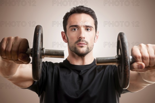 Personal Trainer doing front dumbell raises for training his deltoids in a brown background