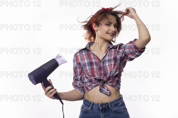 A playful young woman joyfully uses a hair dryer, delighting in her hairstyle with vibrant energy and enthusiasm
