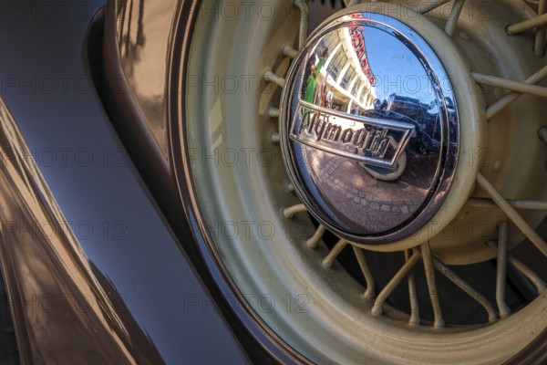 Lisbon, Portugal - Sep 29, 2024: Close-up and selective focus of spare wire wheel and wheel center cap with Plymouth logo on sunny day. Urban setting reflections, vintage look. Plymouth Chrysler motors, Chrysler Corp, USA