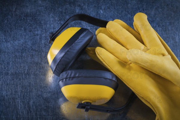 Safety yellow earmuffs and leather construction gloves on scratched metallic surface building concept