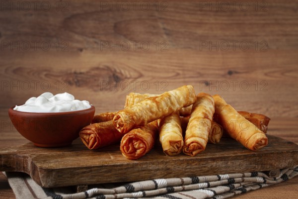 Fried spring rolls with cheese, on a wooden chopping board, with cream sauce, no people