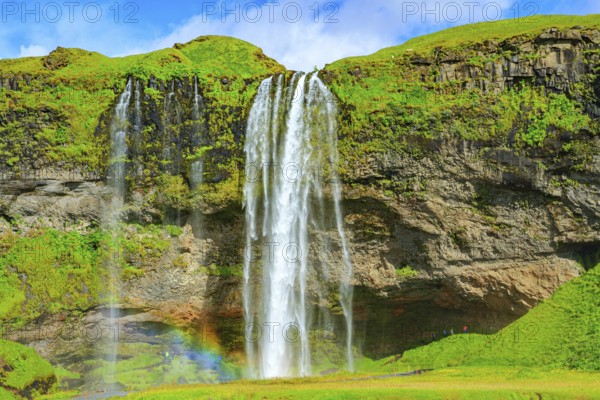 The famous Seljalandsfoss waterfall. Travel to exotic Iceland. Magnificent rainbow appears in the splash of water. Fine July day