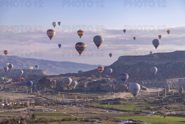 A picture of colorful hot air balloons flying over the landscape of Goreme Historical National Park at sunrise