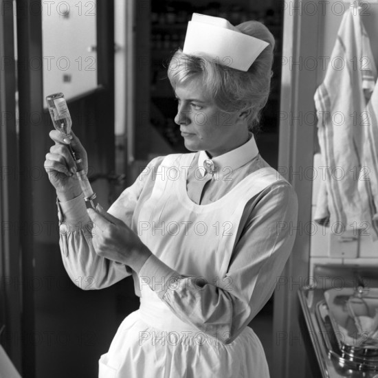 Nurse in the 1960s. A woman in a nurse uniform is preparing an injection and sucks the liquid from a bottle of medicine into a syringe. september 1963