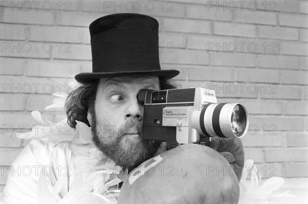 In the 1970s. A man is filming with a amateur film camera. The film was then developed and shown on a film projector on a fold up screen at home. Ricky Bruch (1946-2011) Swedish track and field athlete. He was known for being somewhat of a showman pictured here wearing boxing gloves, a feather boa and a cylinder hat. 1975