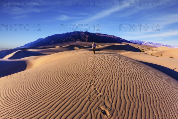 Sunrise in the orange sands of the desert Mesquite Flat, USA. Woman - photographer is among the gently sloping sand dunes