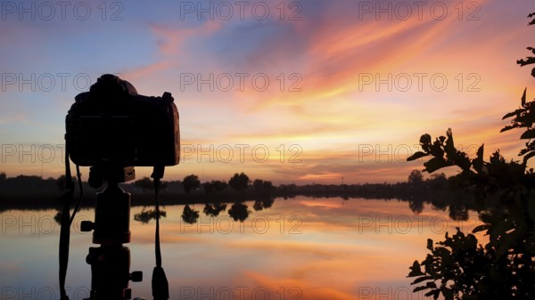 Silhouette of a camera at sunset.Dslr camera shooting on a cityscape sunset with lake reflection