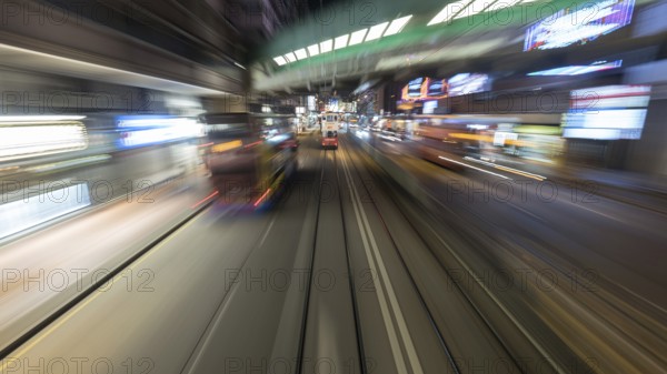 Tarveling through night Hong Kong by double-decker tram. View to road with moving bud and rails with another tram