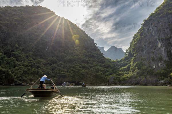 Boats in the river under bright sunlight and green mountains, rowing boats for tourists in Halong Bay in Vietnam