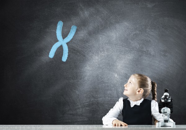 Little girl scientist with microscope on chalkboard background with x chromosome. Research and discovery concept. Elementary science class in modern school. Schoolgirl in schoolwear sitting at desk