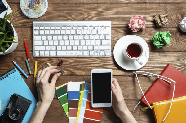 Web designer choosing colors from swatches at wooden desk. Top view office workplace with computer keyboard and stationery. Designing user interface of mobile application. Coloristics in visual design