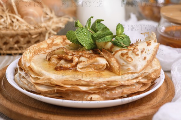 Homemade thin crepe (pancakes) with honey stacked in a stack, on a table with milk and eggs in a basket. Country style food. Traditional Slavonian, pagan holiday Maslenitsa