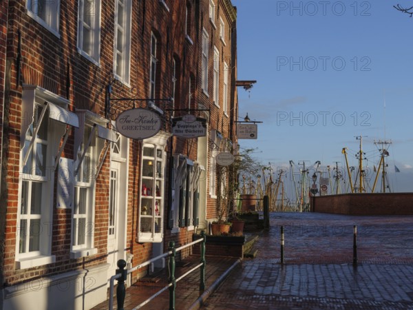 Old town street with traditional buildings, shops and view of the harbour in the winter sun, Greetsiel, East Frisia, Germany