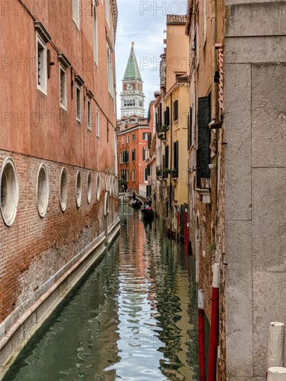 Narrow Venetian canal flanked by historic buildings with the bell tower in the distance. Venice, Italy