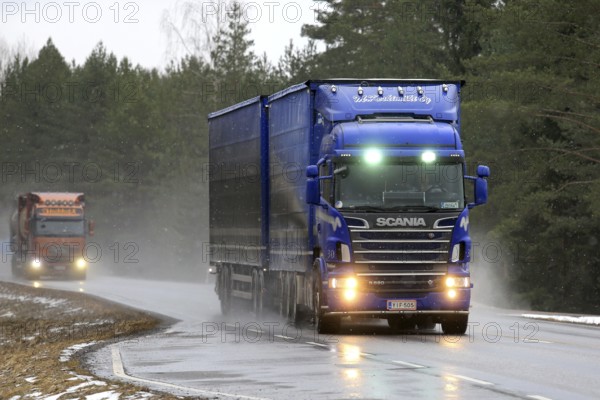 SALO, FINLAND, MARCH 4, 2017: Blue Scania R620 combination vehicle of M. Keskimaki and another truck transport goods along wet road in snowfall