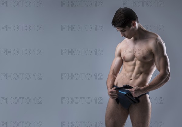 Muscular fit young male antique perfect muscles six packs of abs and bare chest. Bodybuilder model trains with a stretching elastic against a dark background in the studio. Workout training gym
