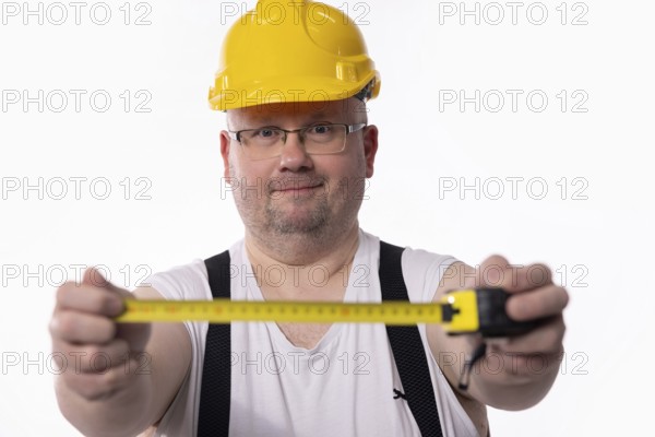 A construction worker in a yellow hard hat measures using a tape measure, showcasing tools of the trade
