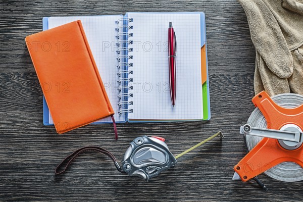 Rolled tape measures safety gloves notebooks pen on wooden board
