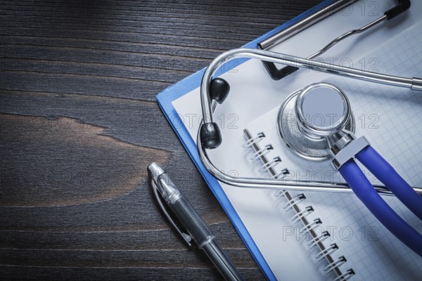Clip board squared notepad pen and medical stethoscope tablet on vintage wooden background medicine concept