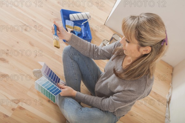 Female holding color palette and paintbrush and sitting on wooden floor