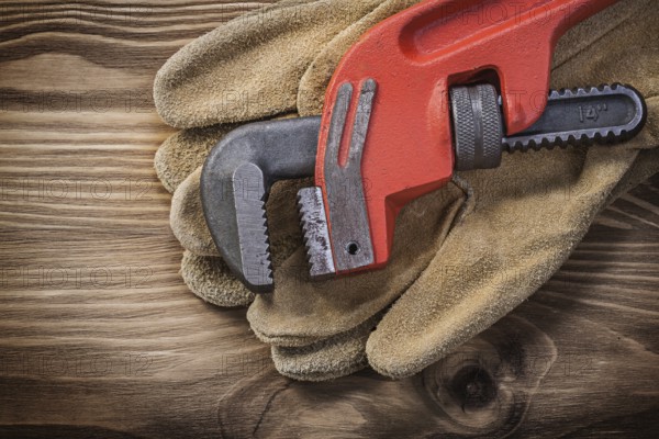 Pair of leather protective gloves pipe wrench on wooden board construction concept