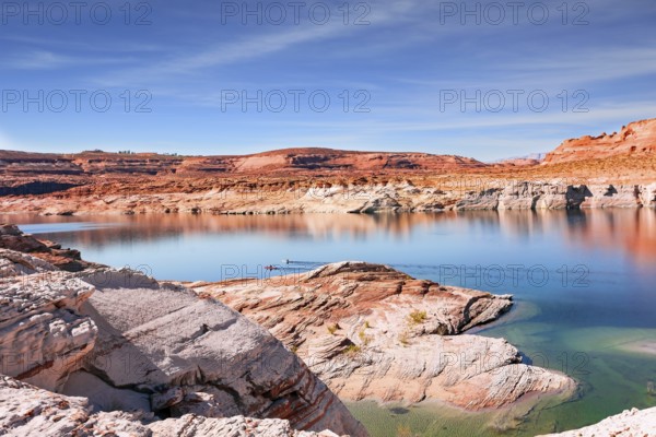 Lake Powell. The water reflects the surrounding shores. The smooth emerald water of the lake contrasts with the bright red terracotta sandstone shores. USA. The coast is cut by narrow canyons