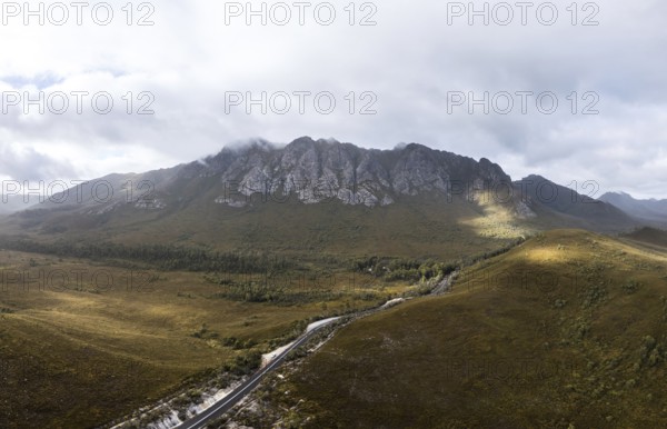 An aerial view of Gordon River Rd at the Sentinel range of mountains near Bitumen Bones Sculpture on a hot summer's afternoon in Southwest National Park, Tasmania, Australia