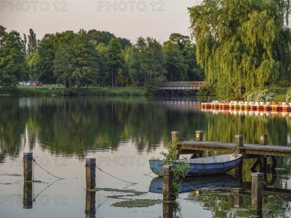 A quiet lake with boats and a jetty, surrounded by green nature at dusk, Pröbstingsee, Borken, Münsterland, Germany